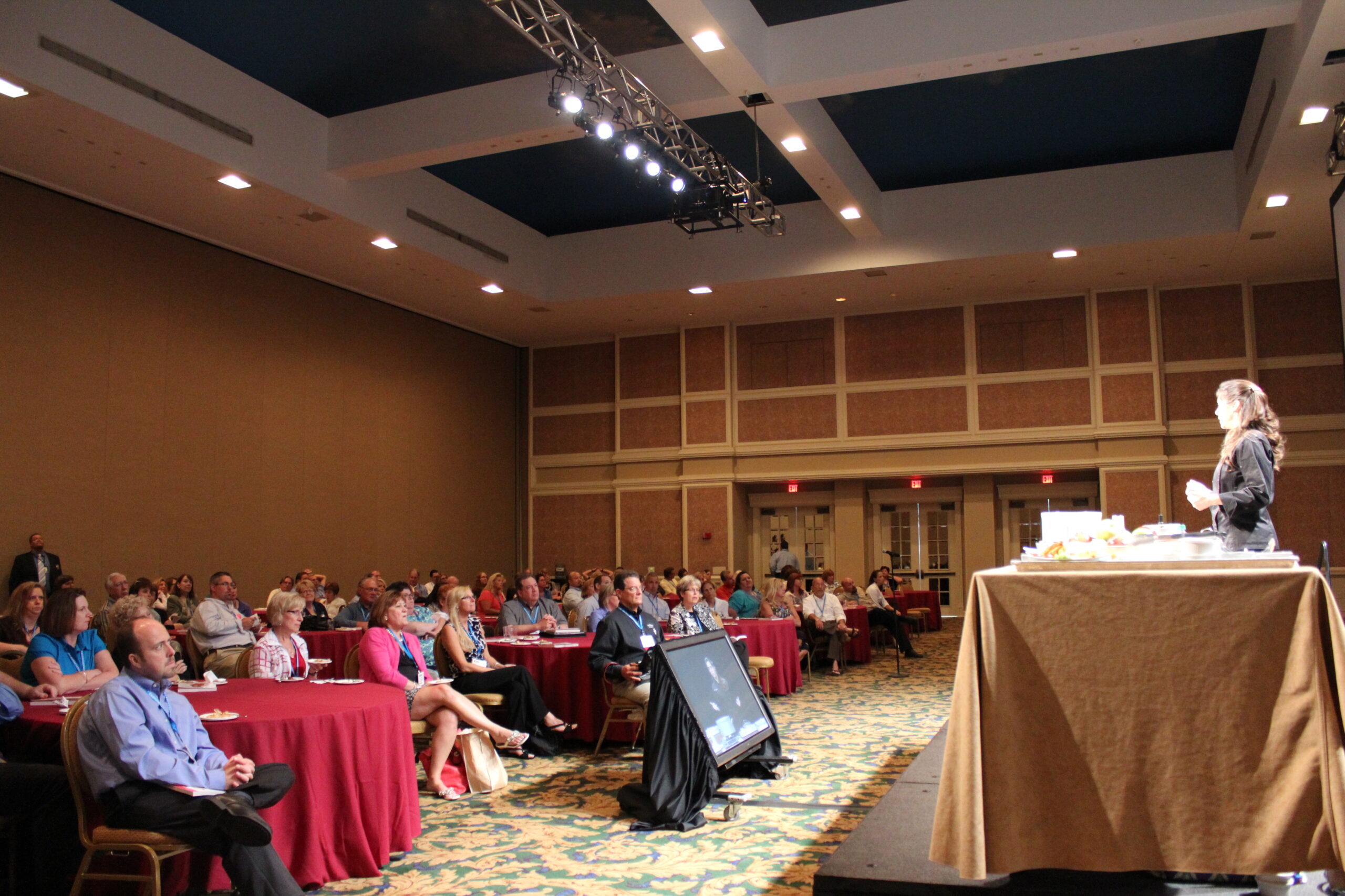 A full corporate audience seated at tables watching Devin Alexander present